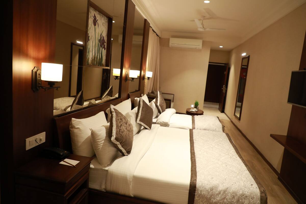 Habitación de hotel con una cama grande, una mesita de noche con lámpara, un espejo y una pequeña mesa con una planta.