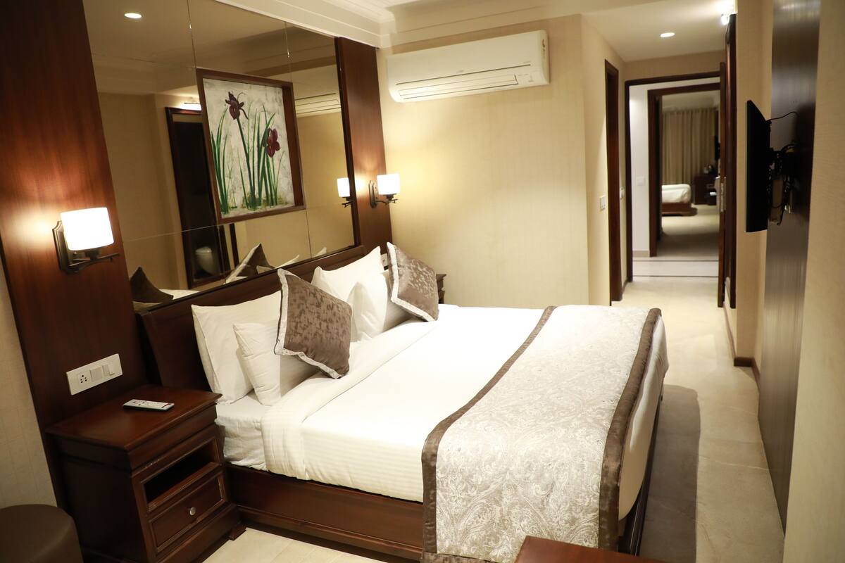 Una habitación de hotel con una cama grande, mesitas de noche, un espejo, un aire acondicionado y un televisor.