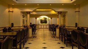 A formal dining area with a long table and chairs, a tiled floor, and a decorative archway in the background. - Hotel Siddhartha Palace (Ahmedabad)