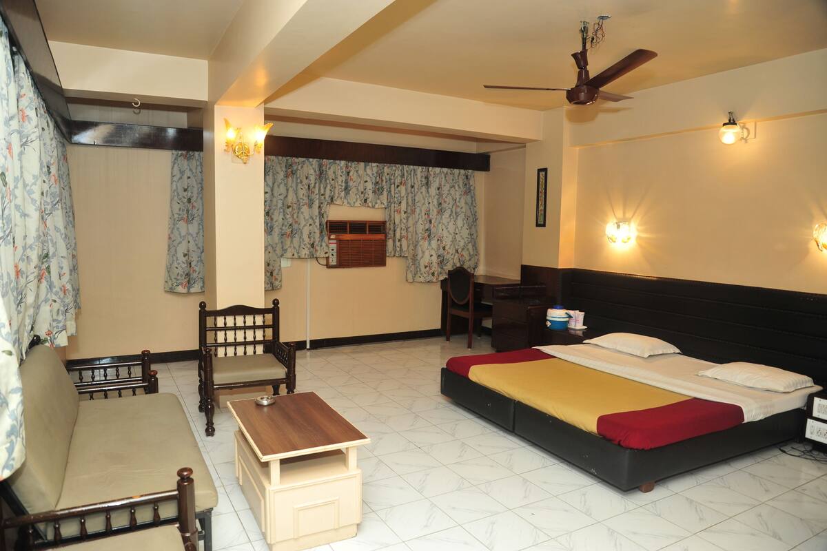 A hotel room with a bed, a desk, a chair, a sofa, and a ceiling fan.