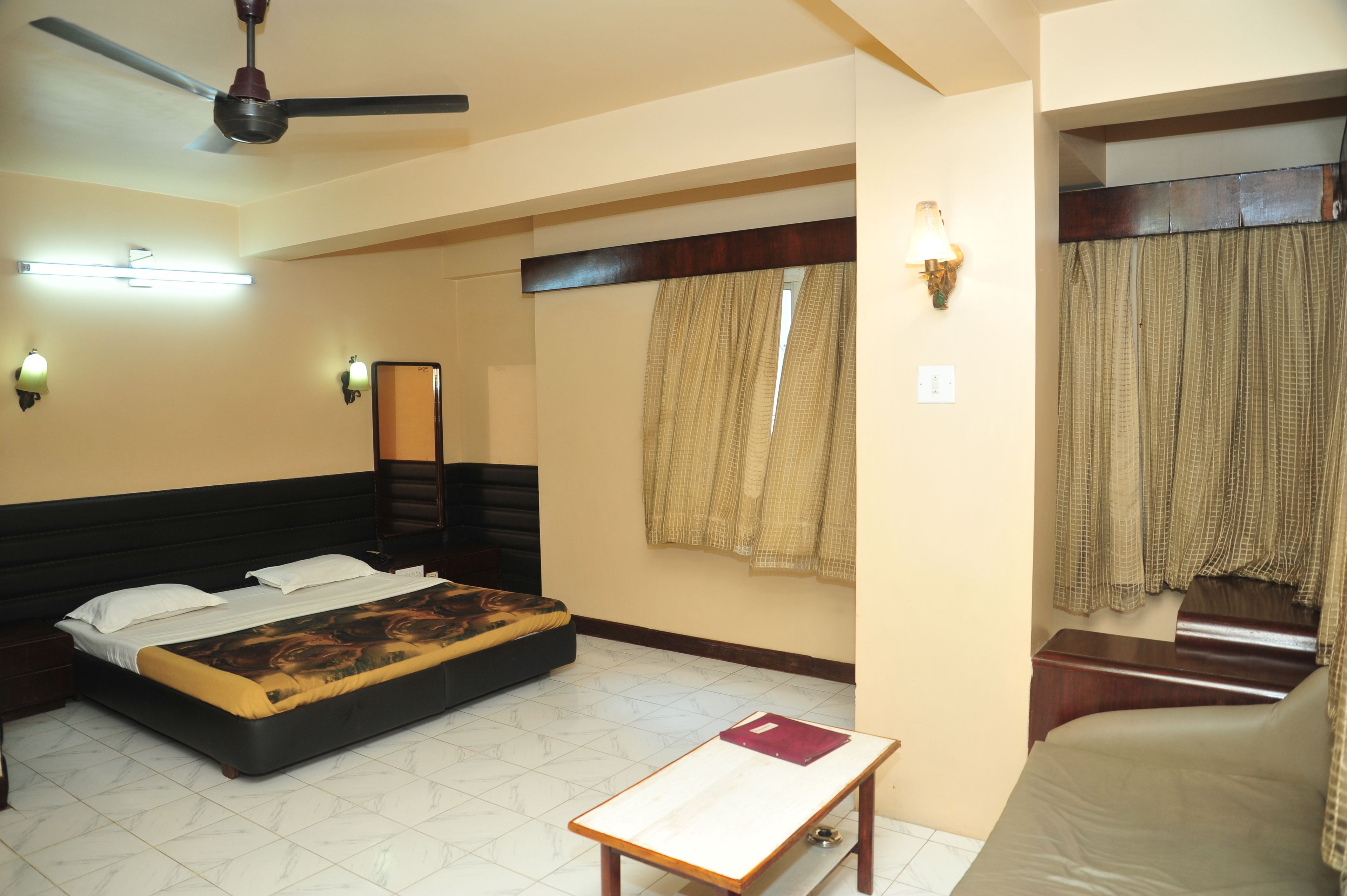 A bedroom with a bed, a ceiling fan, a nightstand, a bedside table, and a window with curtains.