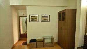 A hallway with a wooden wardrobe, a glass table, and two framed pictures on the wall. - Tiger Inn (Kolkata)