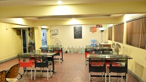 A dining area with tables and chairs, water dispensers, and a Buddha statue on the wall. - Tiger Inn (Kolkata)