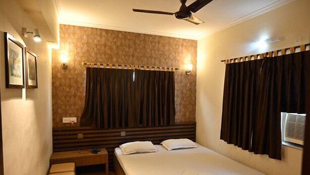 A hotel room with a bed, bedside table, and a ceiling fan. - Tiger Inn (Kolkata)
