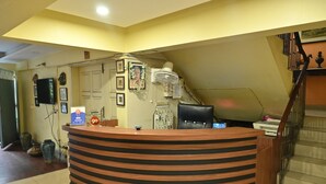 A reception desk with a striped design, a mounted television, framed pictures, a fan, and a staircase to the right. - Tiger Inn (Kolkata)