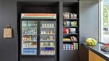 A vending machine stocked with beverages and snacks, a paper bag hanging on the wall, and a window with a view of the outside.