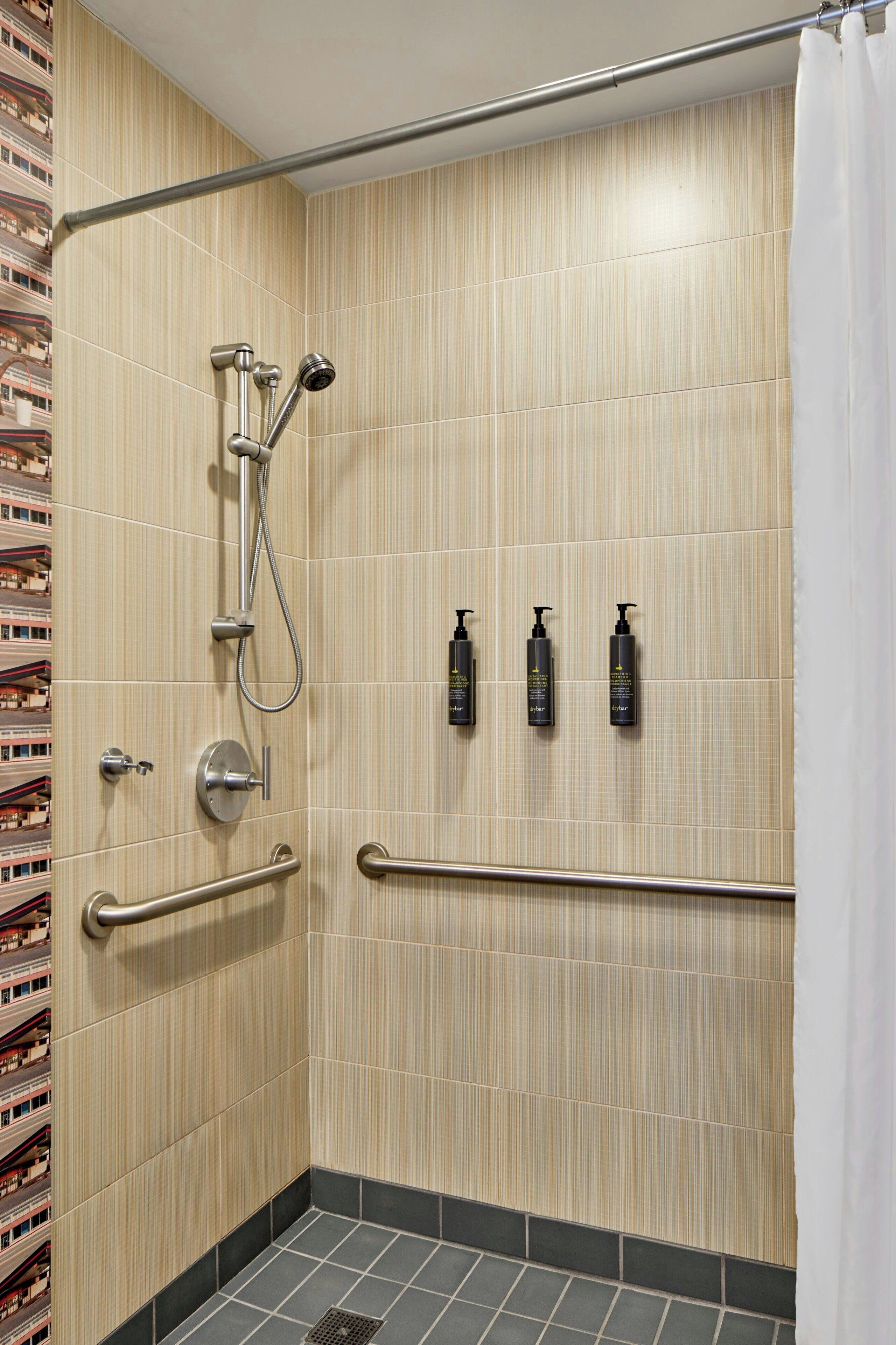 A shower area with a handrail, a showerhead, and three bottles of shampoo.