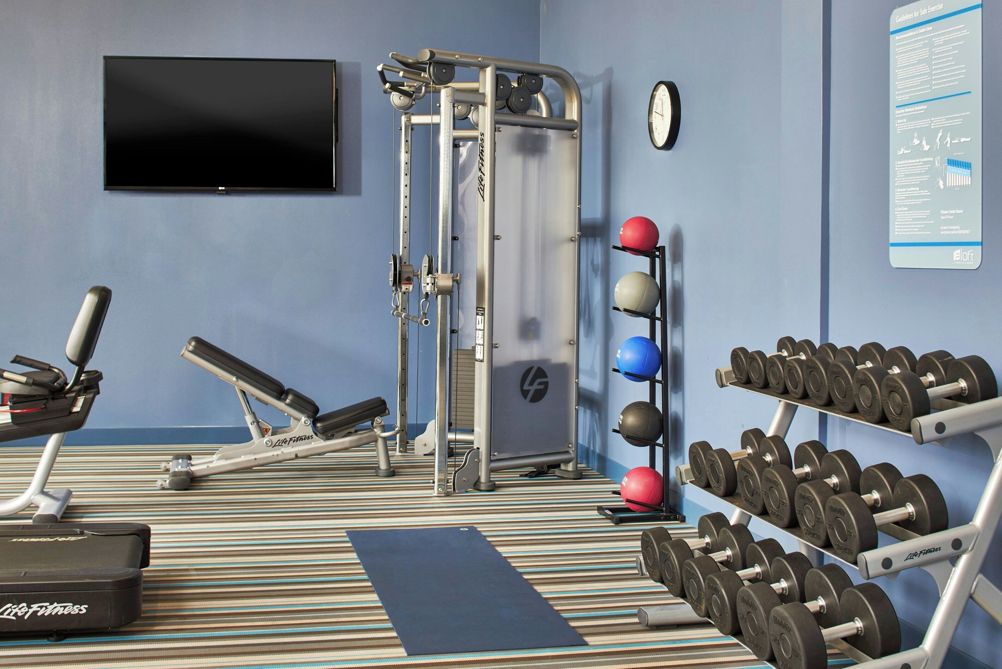 A gym with exercise equipment, dumbbells, and a wall-mounted TV.