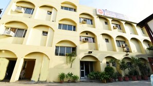 A multi-story building with a yellow facade, multiple balconies, and a sign advertising a hotel booking service. - Hotel Raj Darbar (Amritsar)