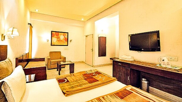 A hotel room with a bed, a chair, a desk, a television, and a painting on the wall. - Hotel Raj Darbar (Amritsar)