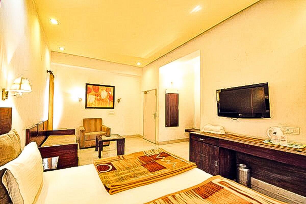 Una habitación de hotel con cama, una silla, un escritorio, un televisor y un cuadro en la pared.