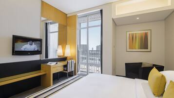 A hotel room with a bed, a desk, a television, and a window with a city view.
