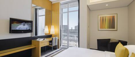 A hotel room with a bed, a desk, a television, and a window with a city view.