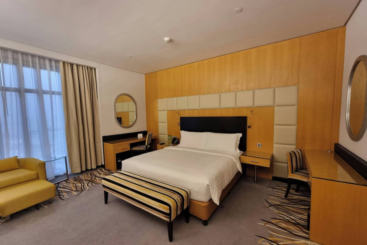 A hotel room with a large bed, a desk, a chair, a mirror, and a window with curtains.