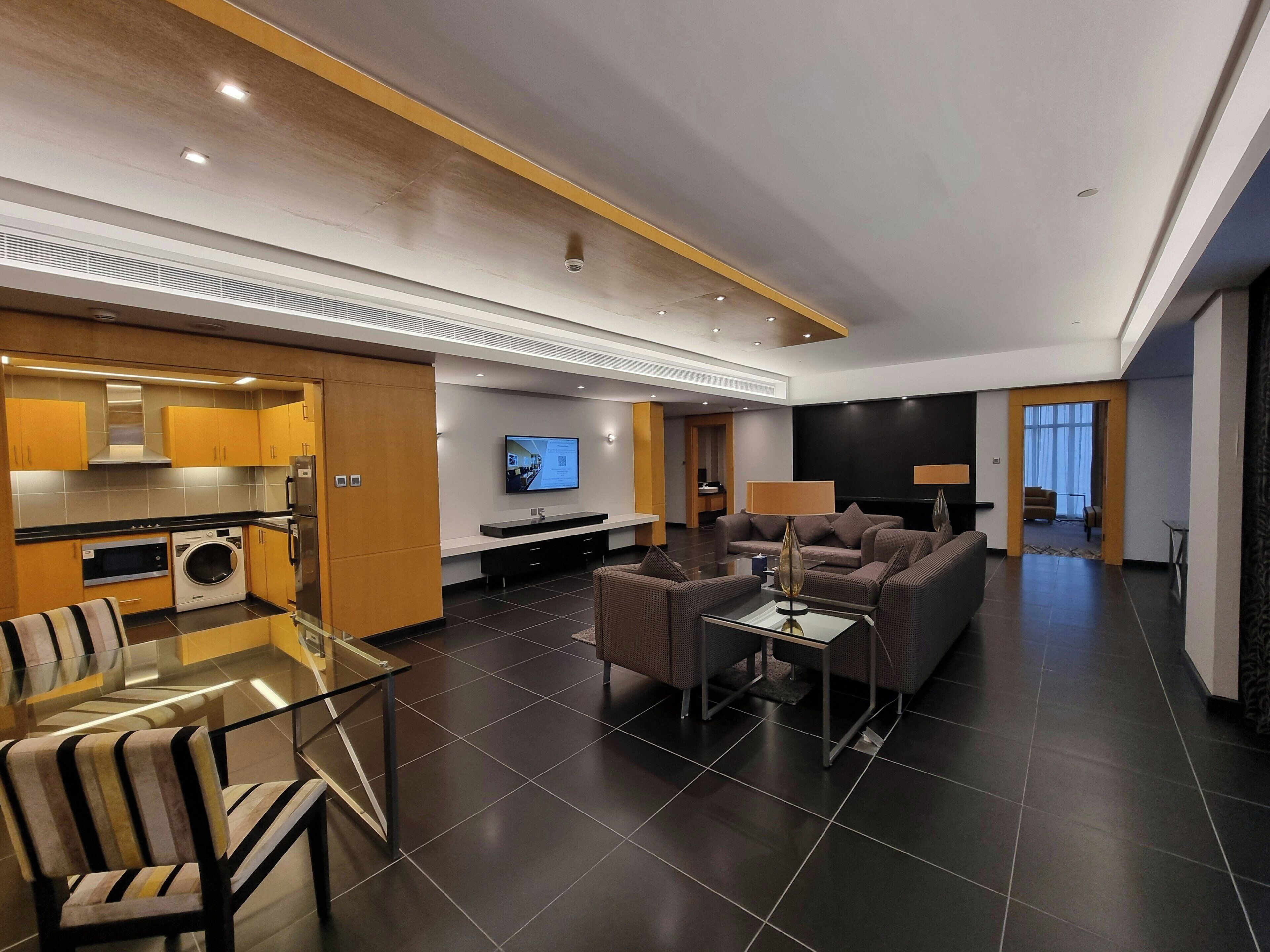 A modern living room with a sofa, a TV, and a kitchen area with a washing machine.