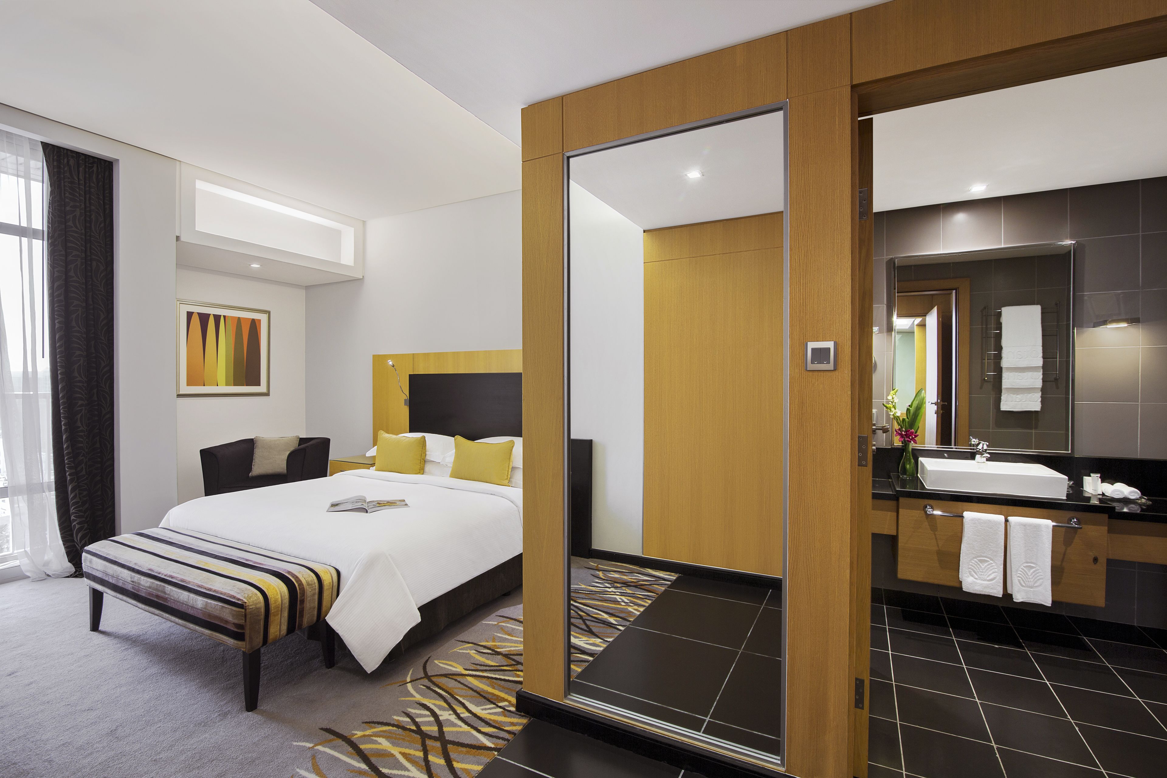 Una habitación de hotel moderna con una cama grande, un baño separado con espejo y vistas a la ciudad.