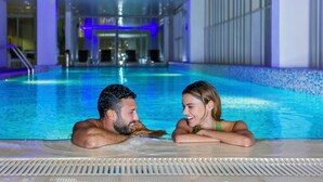 A couple in a modern indoor pool with clear water, surrounded by a tiled floor and glass walls. - Hala Arjaan by Rotana (Abu Dhabi)