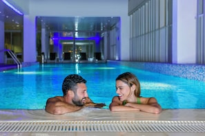 A couple in a modern indoor pool with clear water, surrounded by a tiled floor and glass walls. - Hala Arjaan by Rotana (Abu Dhabi)