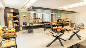 A modern hotel breakfast area with a buffet, a coffee station, and a fruit display. - Hala Arjaan by Rotana (Abu Dhabi)