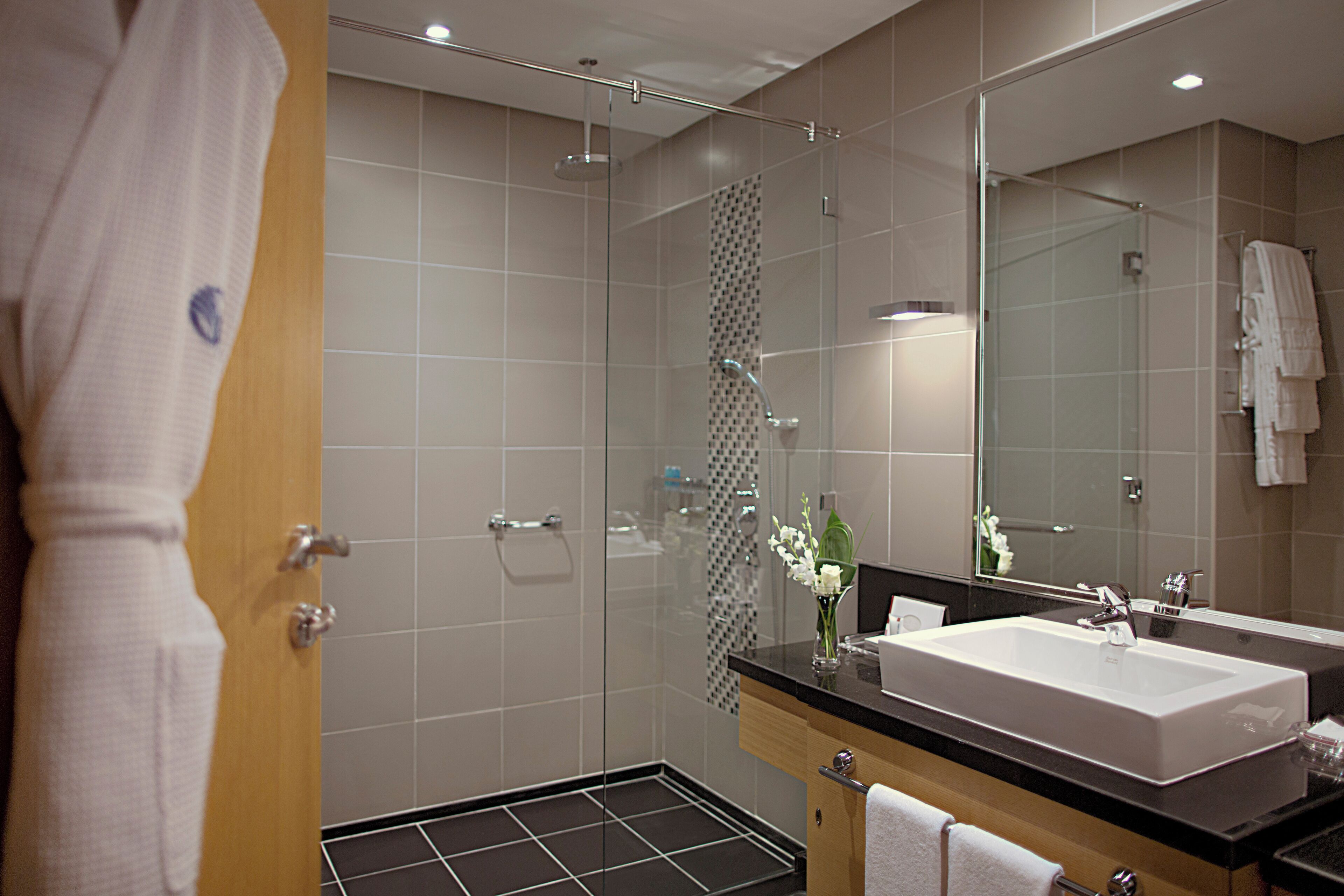 Un baño moderno con ducha envuelta en vidrio, un espejo grande y un mueble de tocador doble.