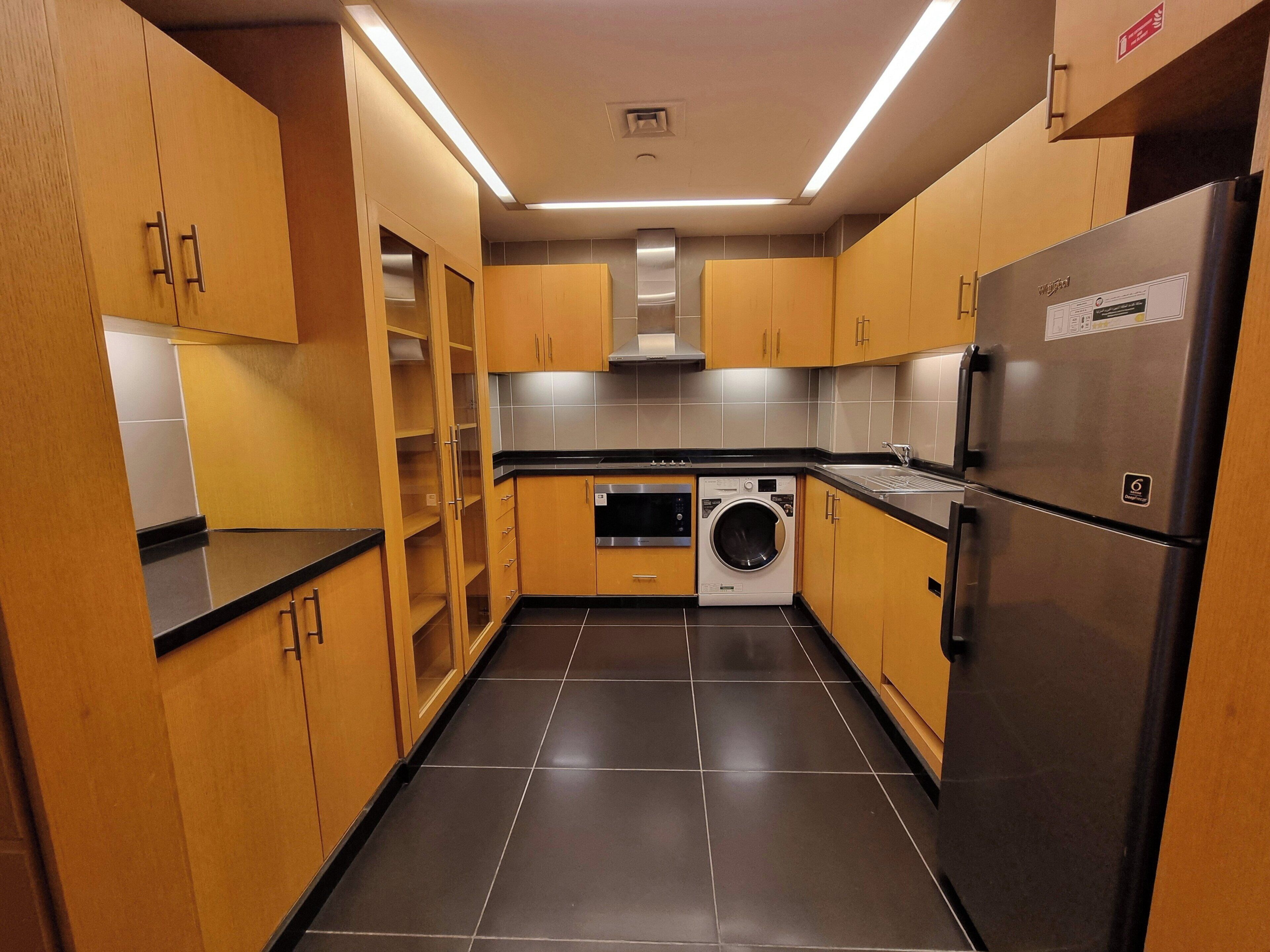 Eine moderne Küche mit Holzschränken, einem Edelstahl-Kühlschrank, einer Waschmaschine und einem Einbauofen.