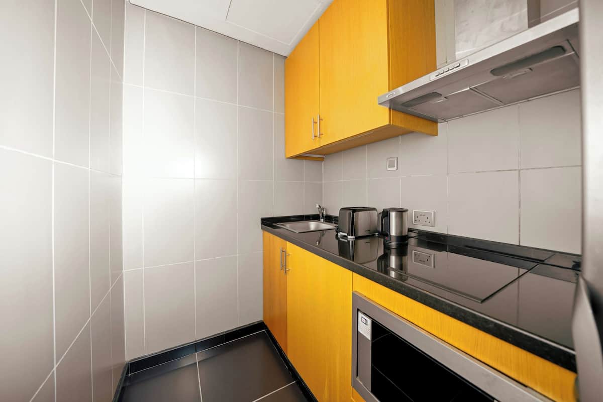 A kitchen with white tiled walls, a black countertop, and wooden cabinets.