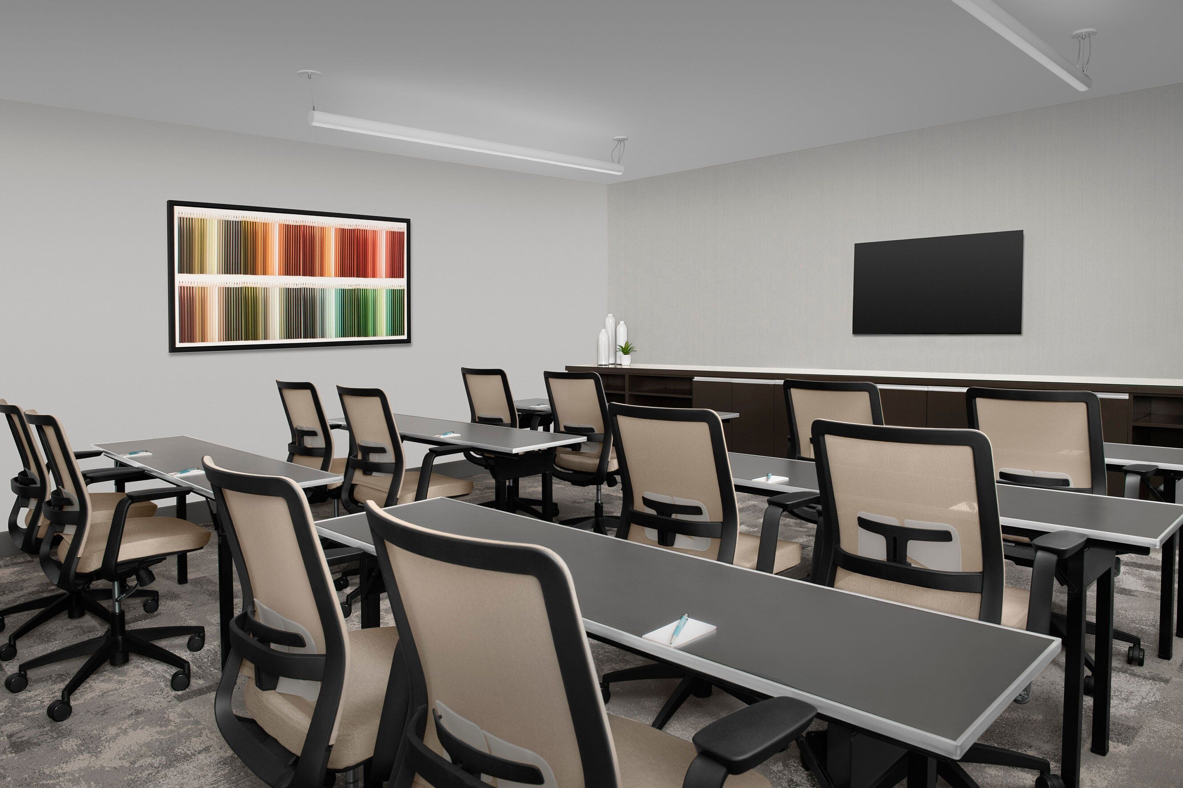 A conference room with a long table, chairs, a projector screen, and a color chart on the wall.