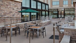 An outdoor patio area with stone walls, multiple tables and chairs, and string lights. - Element by Marriott Denver Park Meadows (Lone Tree)