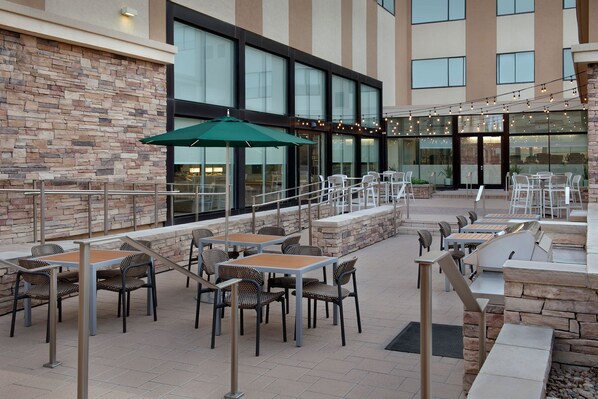 An outdoor patio area with stone walls, multiple tables and chairs, and string lights.