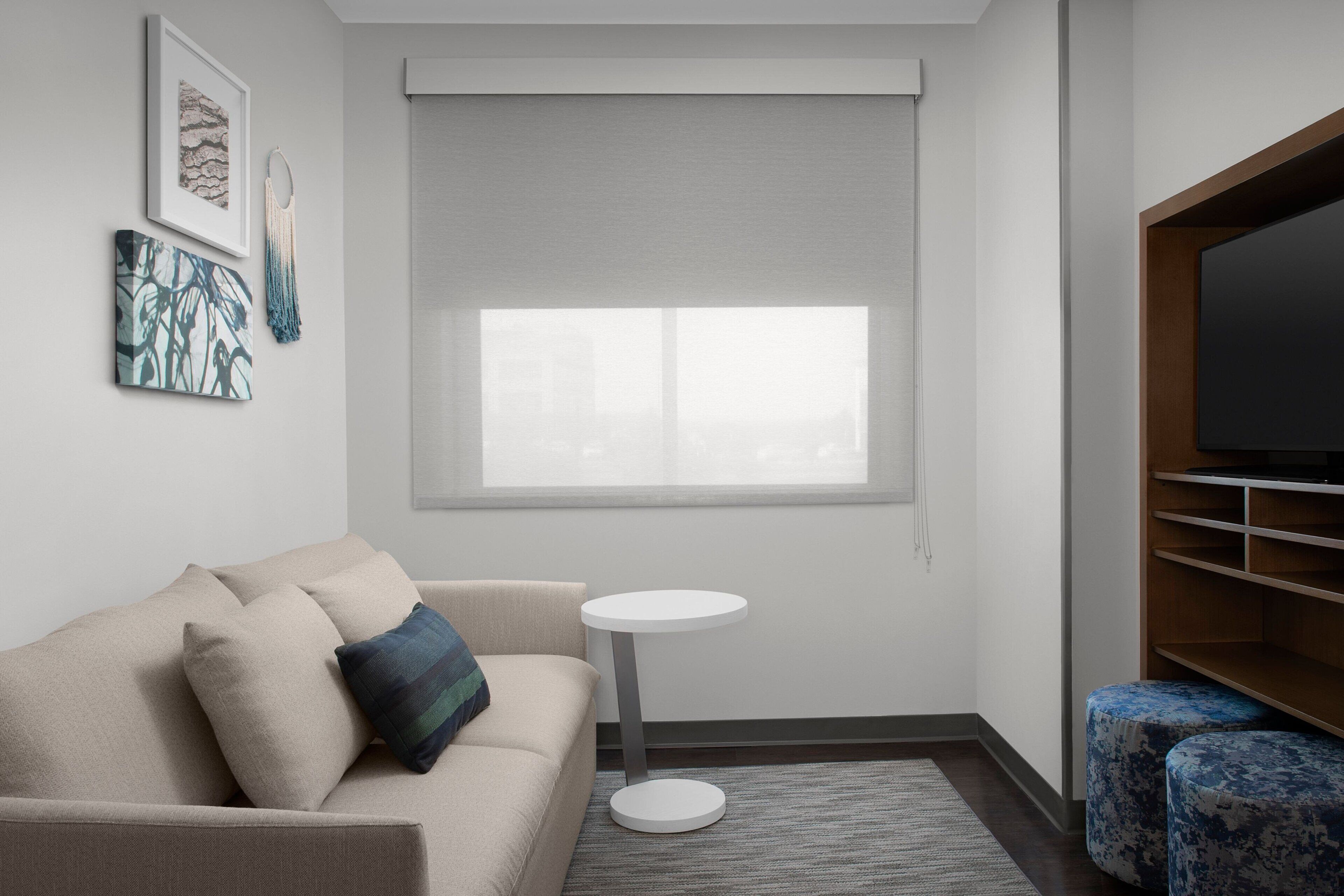 Een moderne woonkamer met een beige bank, een rond witte bijzettafeltje en een televisie op een houten dressoir.