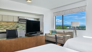 A modern hotel room with a kitchenette, a flat-screen TV, a sofa, a bedside table, and a large window offering a scenic view. - Element by Marriott Denver Park Meadows (Lone Tree)