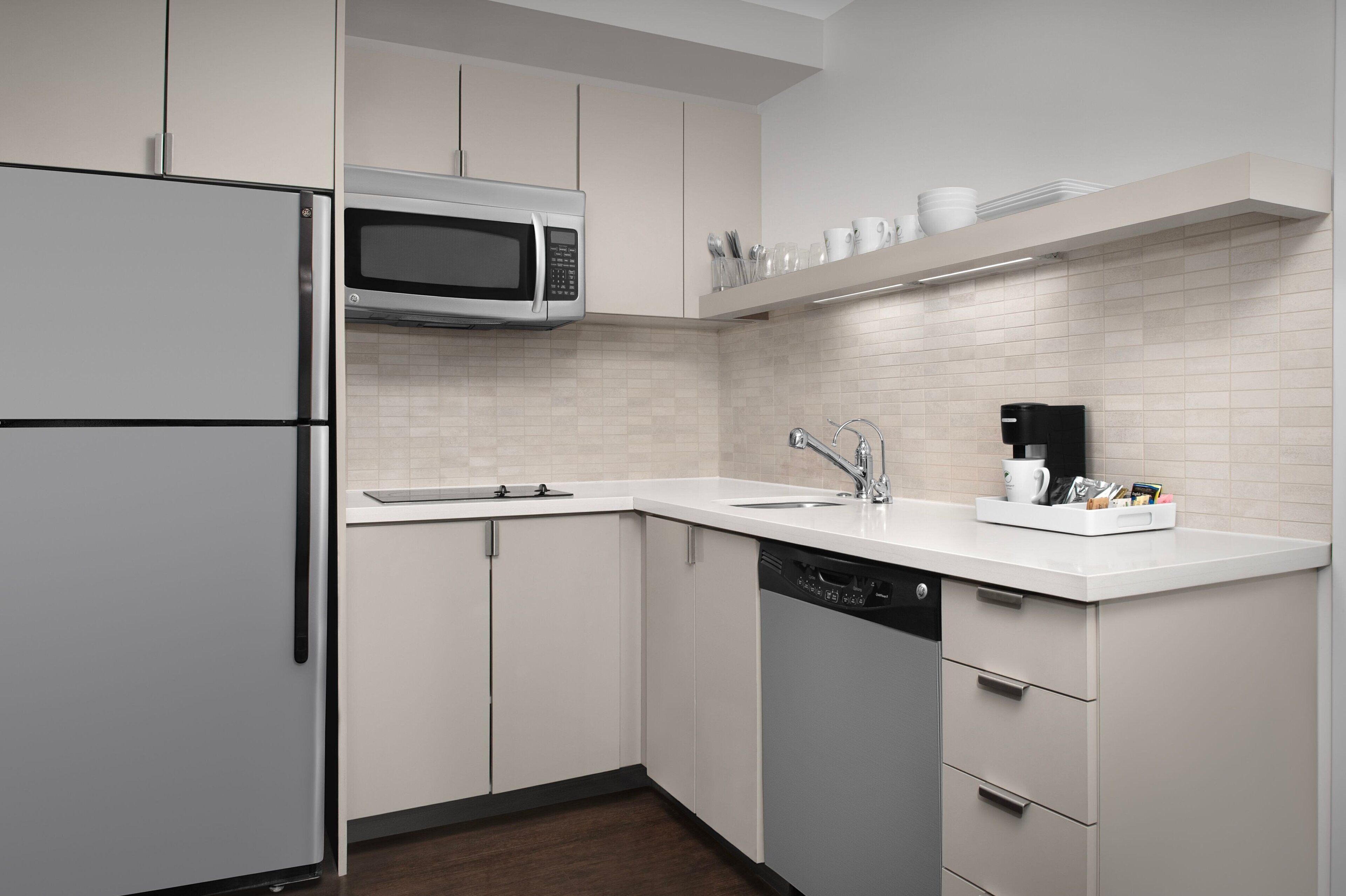 A modern kitchen with white cabinetry, a built-in microwave, a dishwasher, and a coffee maker on the countertop.