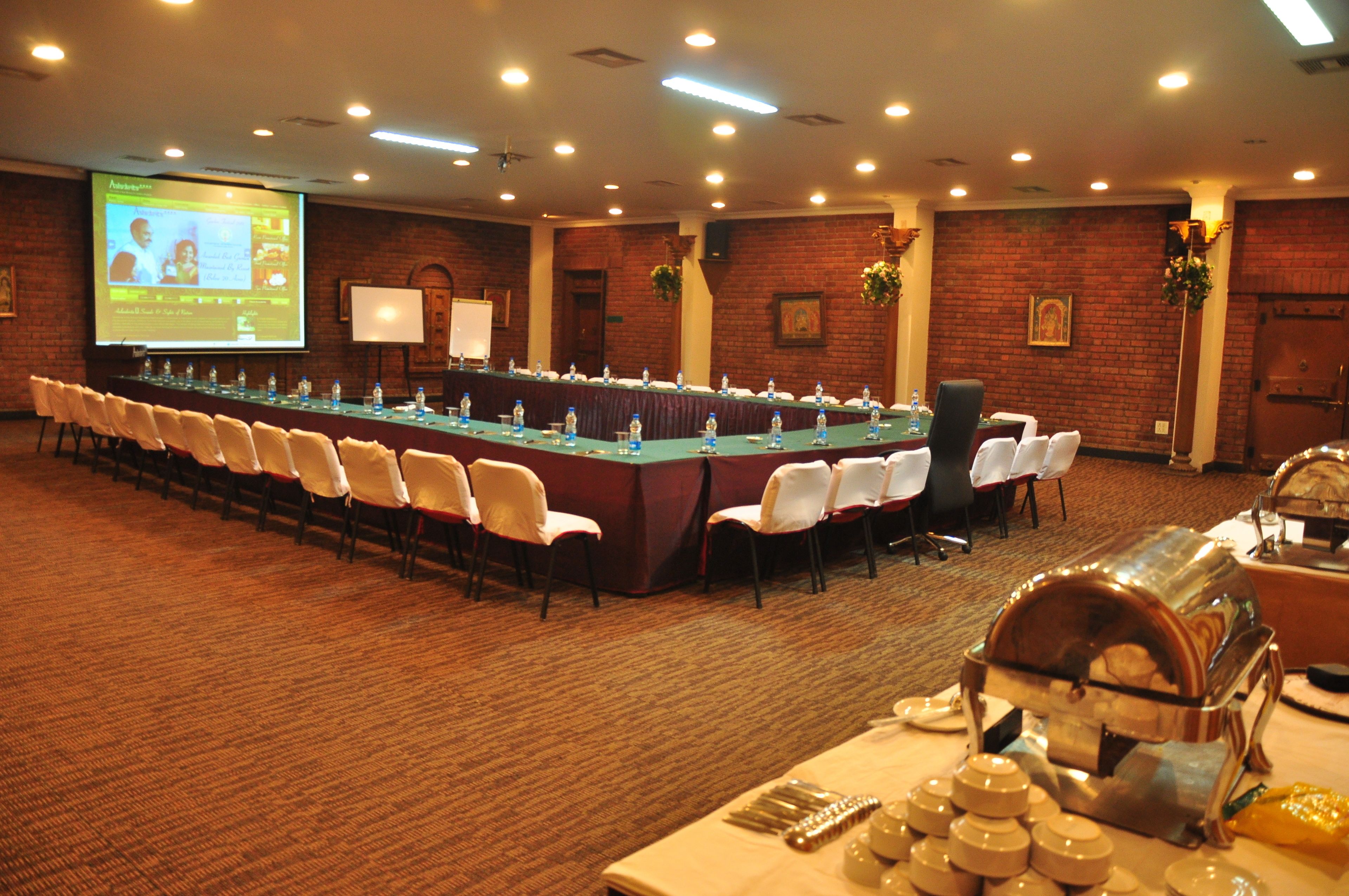 A conference room with a long table, chairs, a projector screen, and a buffet area.