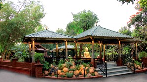 Ein Pavillon mit einer Buddha-Statue, umgeben von einem angelegten Garten mit Steinen und Pflanzen.