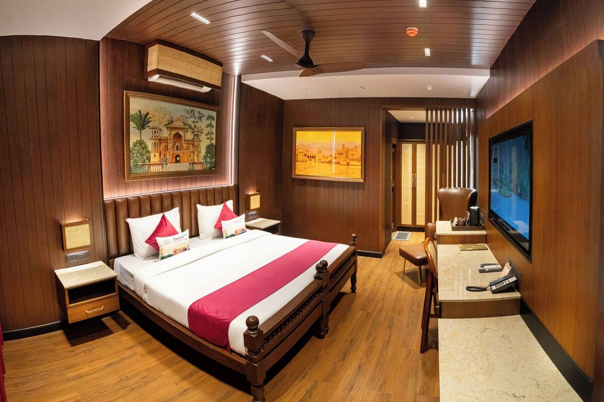A hotel room with a large bed, wooden paneling, a television, a desk, and a painting on the wall.
