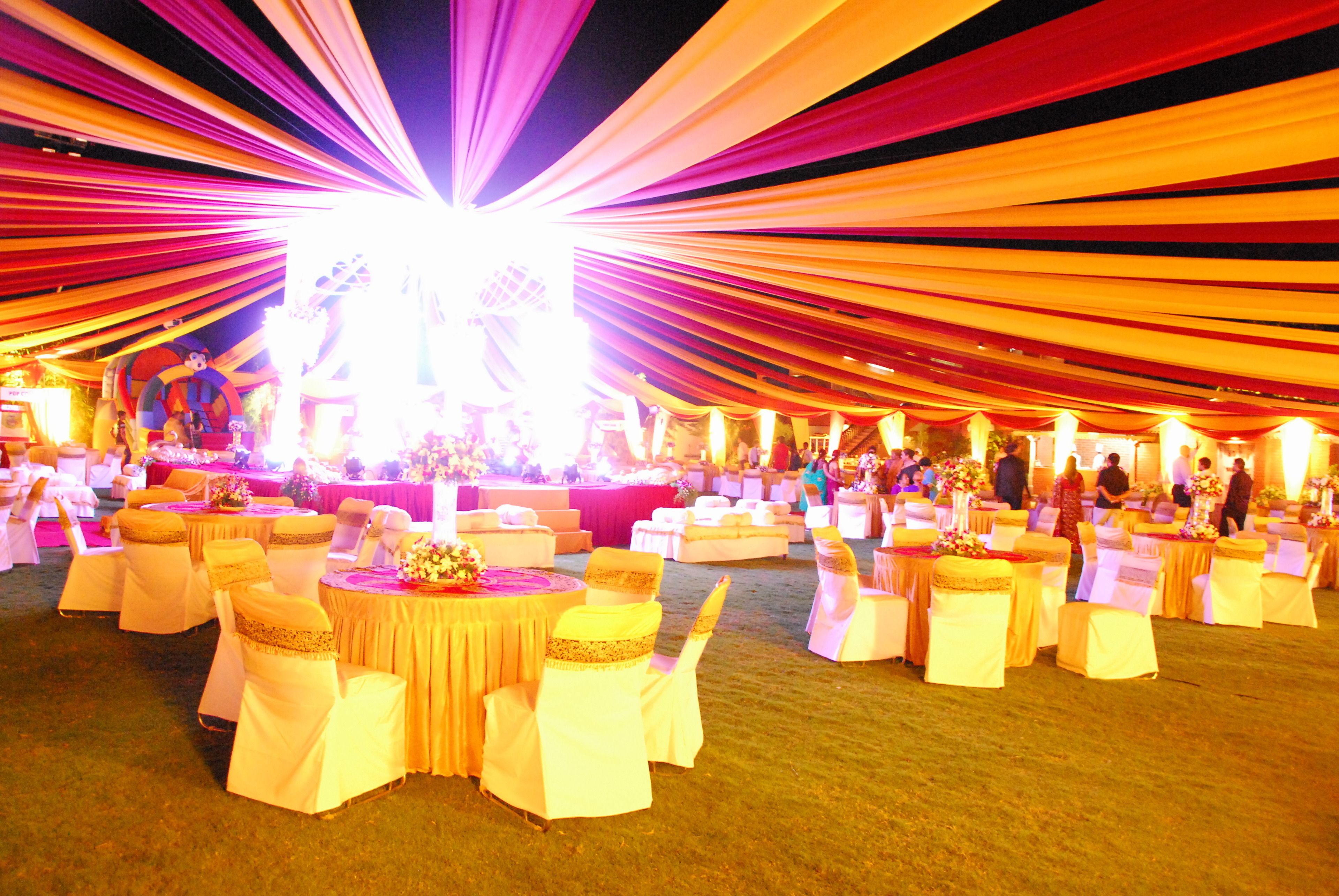 A tented event space with round tables and chairs, decorated with draped fabric and floral centerpieces.