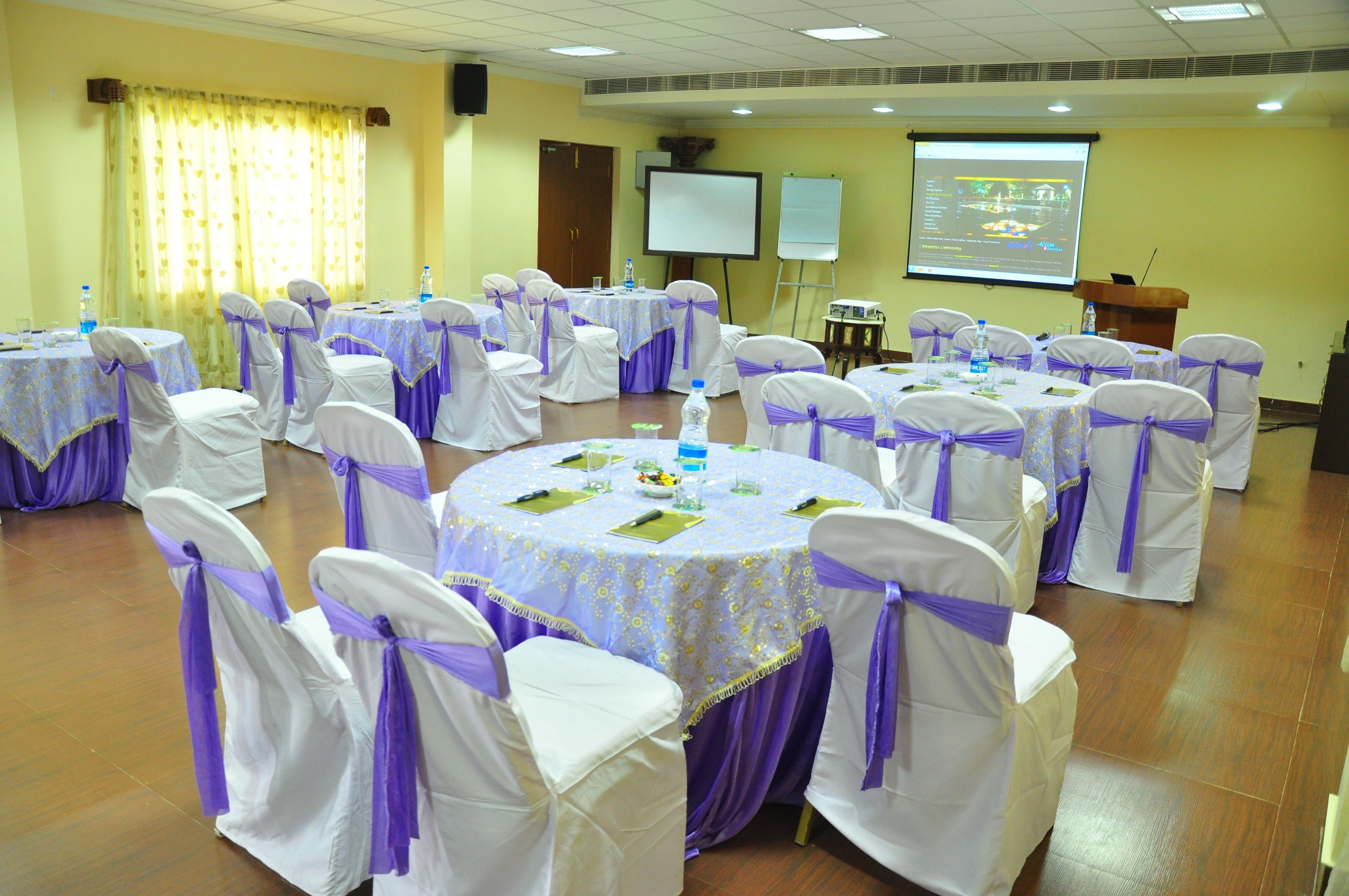 A conference room with round tables and chairs, a projector screen, and a presentation screen.