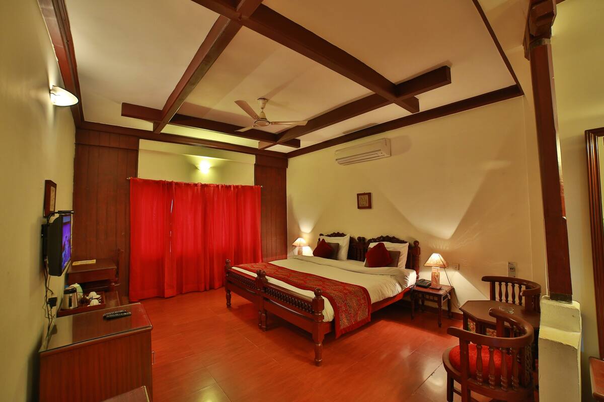 A bedroom with a wooden bed, a desk, a chair, a TV, and a red curtain.