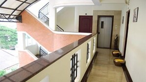 A hotel corridor with a tiled floor, a red door at the end, and a staircase with a metal railing. - Shylee Niwas Kodambakkam I (Chennai)