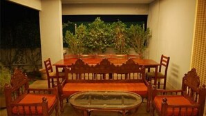 A dining area with a wooden table and chairs, a glass-top coffee table, and potted plants. - Shylee Niwas Kodambakkam I (Chennai)
