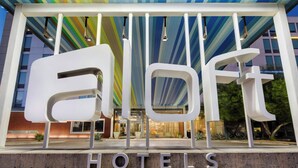 A hotel entrance with a modern design, featuring large white letters spelling "HOTEL" and a colorful striped ceiling. - Aloft by Marriott Phoenix-Airport (Phoenix)