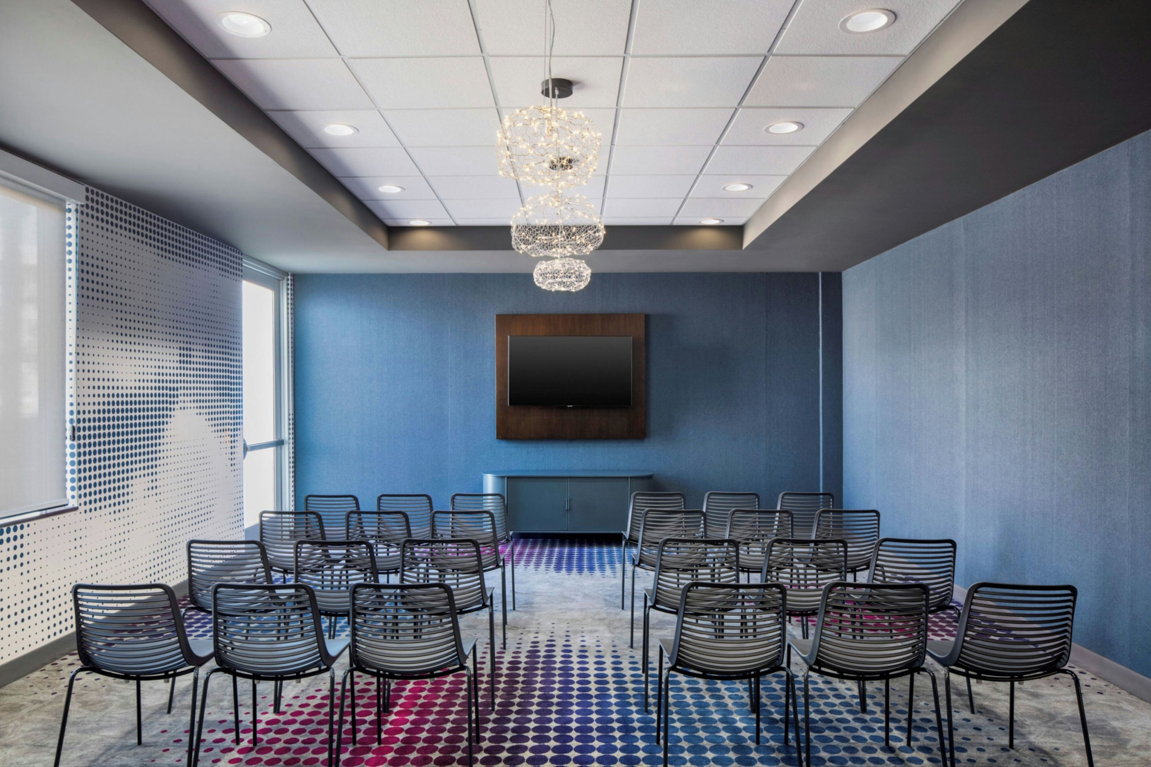 Une salle de conférence dotée d’un grand écran, de nombreuses chaises, d’une moquette à motifs et d’un lustre.