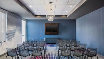 Une salle de conférence dotée d’un grand écran, de nombreuses chaises, d’une moquette à motifs et d’un lustre.