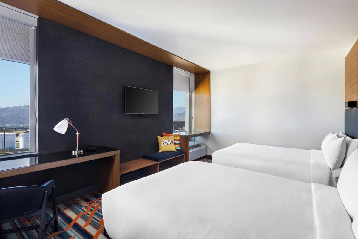 Una habitación de hotel con cama, escritorio, silla, televisión y ventana con vista a la ciudad.