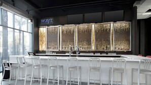A modern bar area with a long counter, white bar stools, and a large illuminated display. - Aloft by Marriott Phoenix-Airport (Phoenix)