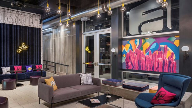 A modern lounge area with a sofa, armchair, and coffee table, featuring a neon sign, artwork, and industrial-style lighting. - Aloft by Marriott Phoenix-Airport (Phoenix)