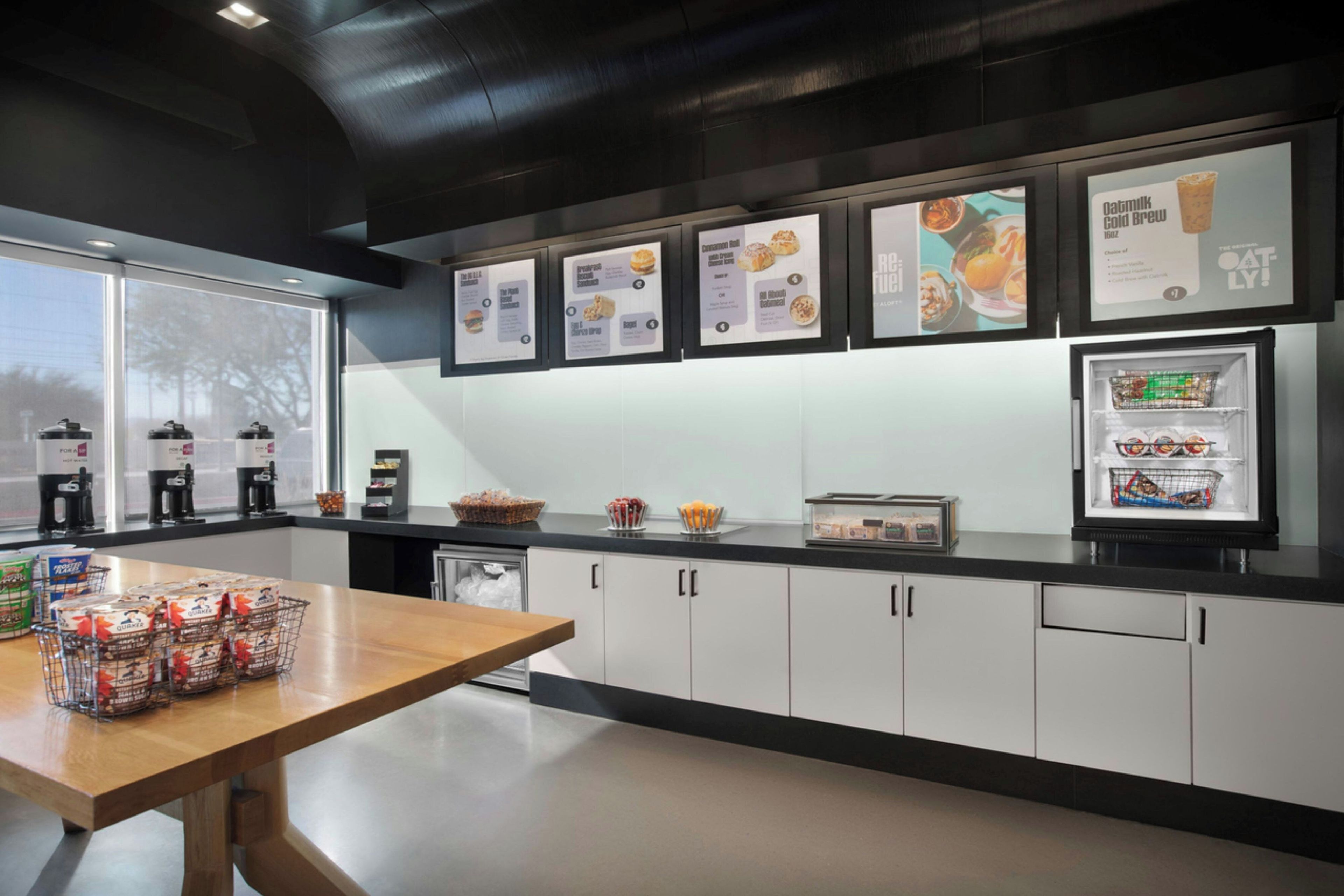 A modern kitchen with a wooden table, coffee machines, and a refrigerator stocked with food.