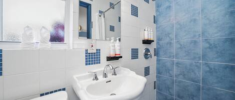Un baño con lavamanos blanco, un espejo y una zona de ducha.