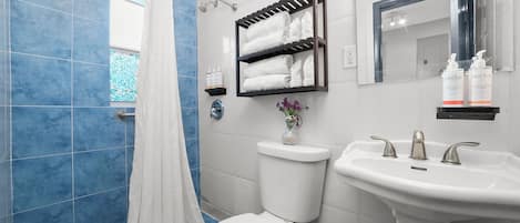 Un baño con inodoro blanco, un lavabo con dos grifos, un perchero con toallas dobladas y un espejo sobre el lavabo.