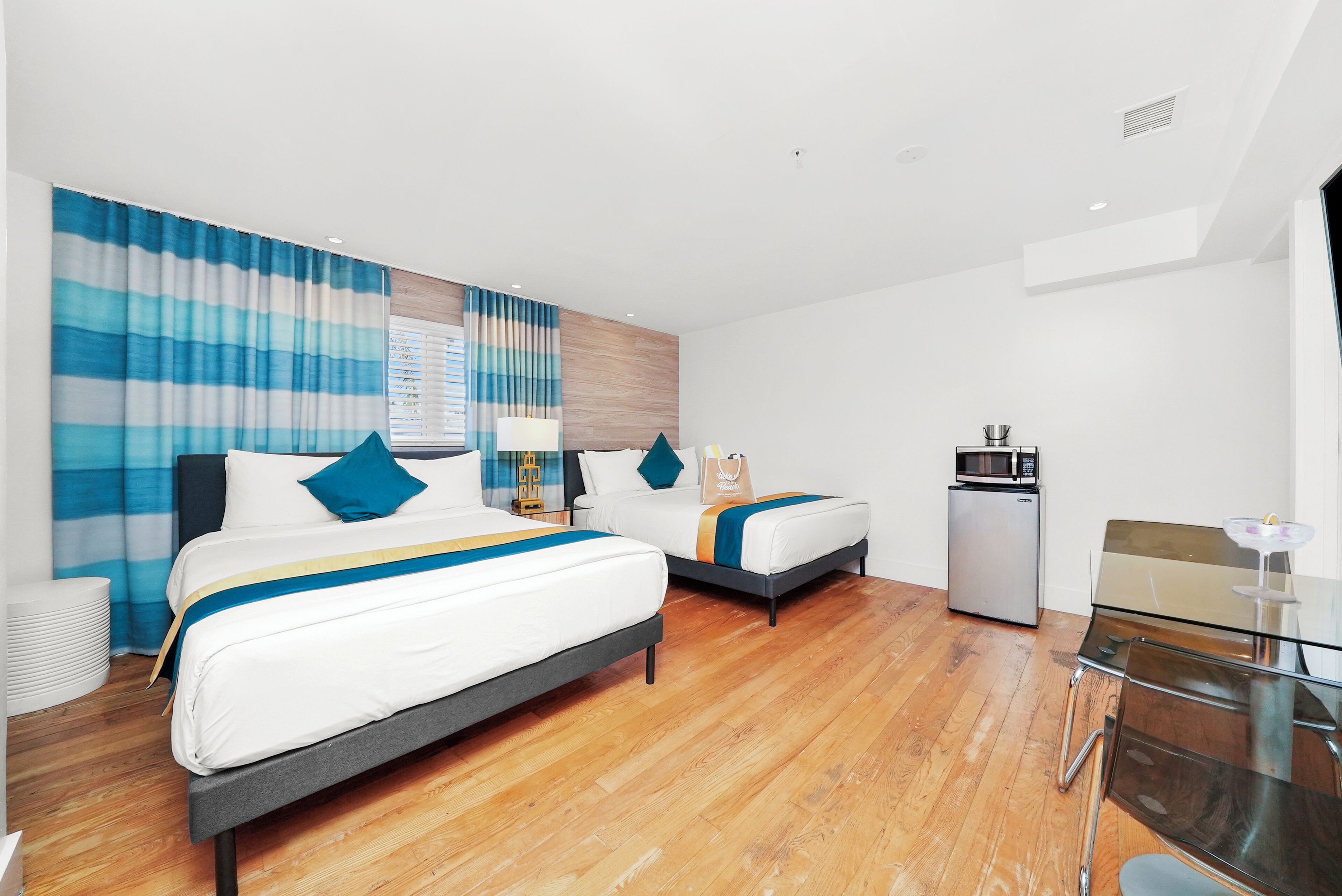A hotel room with two beds, a small kitchenette, and a glass dining table.